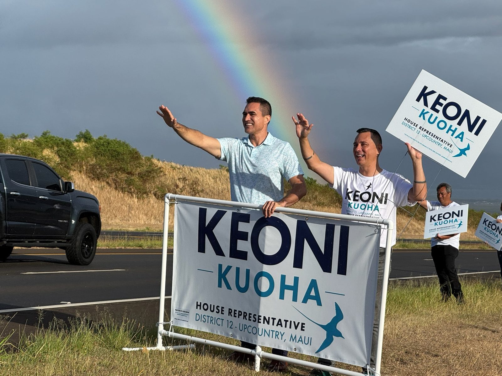 Keoni and supporters sign waving under a rainbow