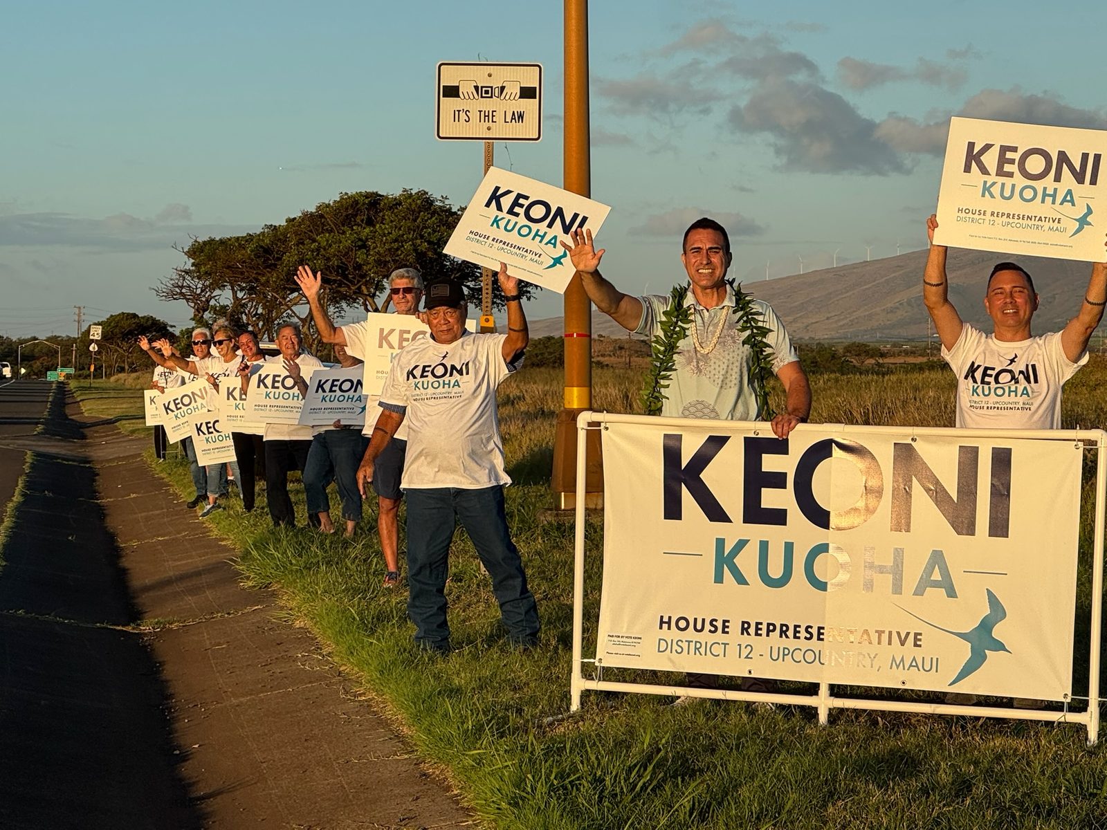 A line of volunteers waving Keoni Kuoha signs along the roadside